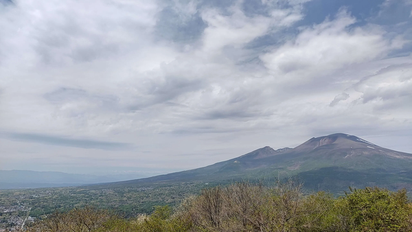Landscape photo of Mount Asama's peak rising above a forested valley under a cloudy blue sky in Nagano.